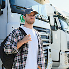 Junger angehender Lkw-Fahrer mit Rucksack vor einer Reihe Lastwagen