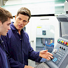 Facharbeiter weist einen jungen Auszubildenden an einer CNC-Maschine ein